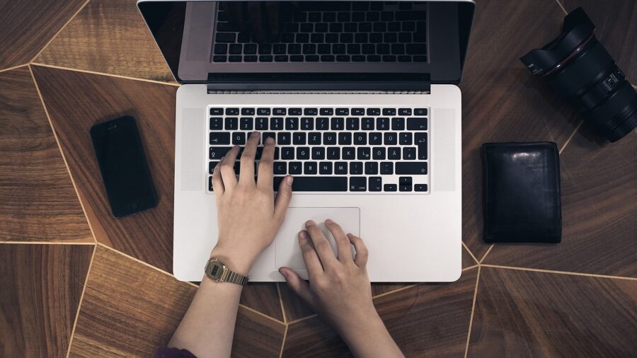 ręce na klawiaturze laptopa położonego na biurku, widziane z góry